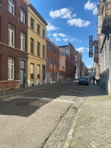A picture of a long street during the day. The small buildings on the left are orange, yellow and other redish colors and they are in the shade.